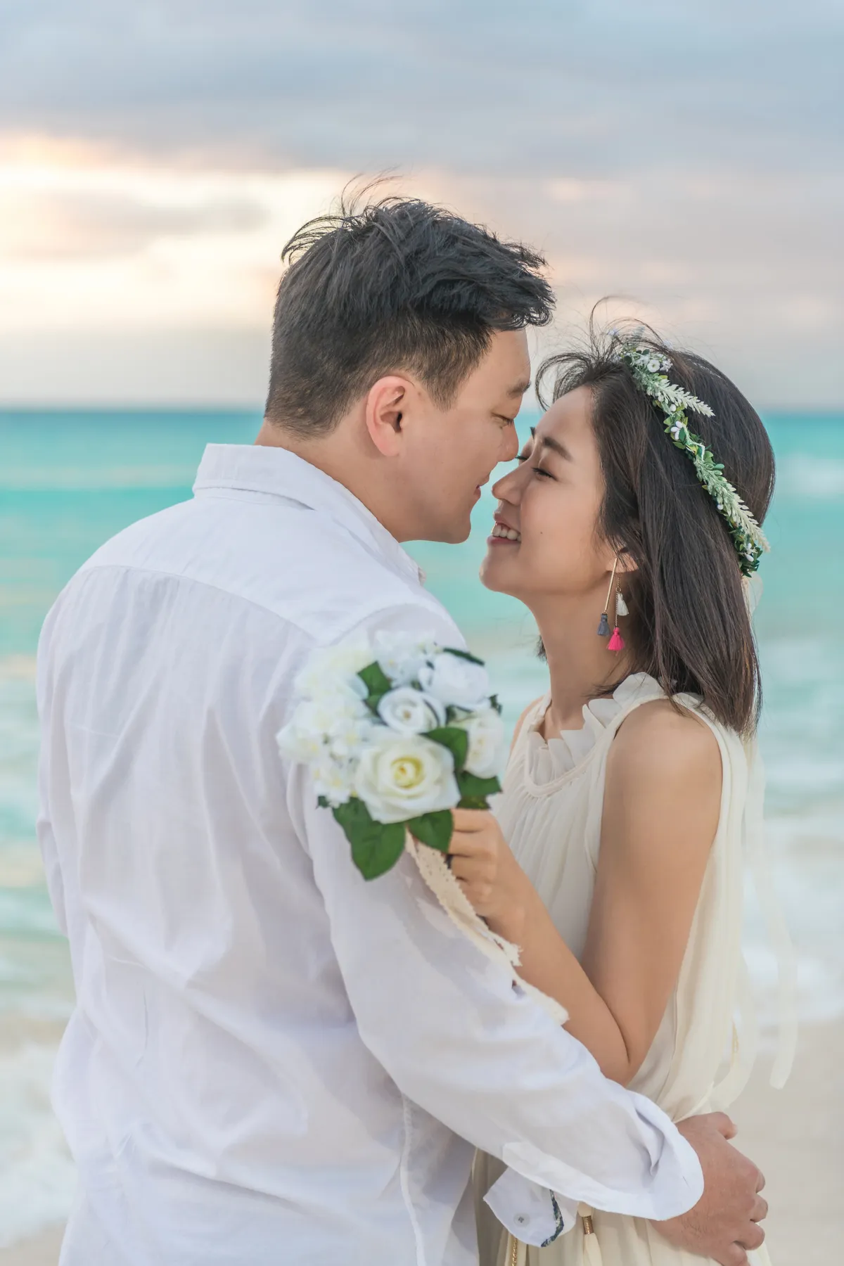 Bride with a bouquet kissing the groom on the beach