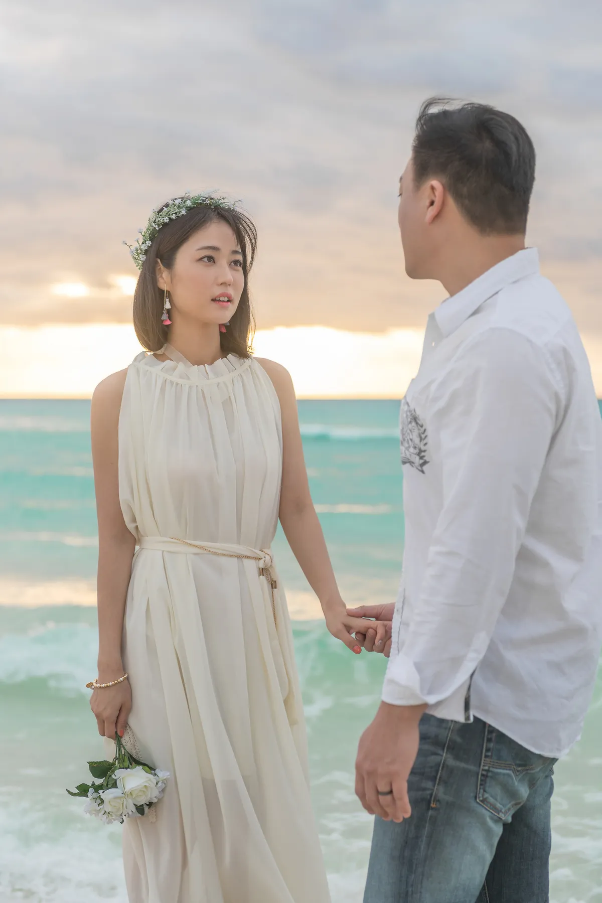 Bride in a flower crown looking at the groom on the beach