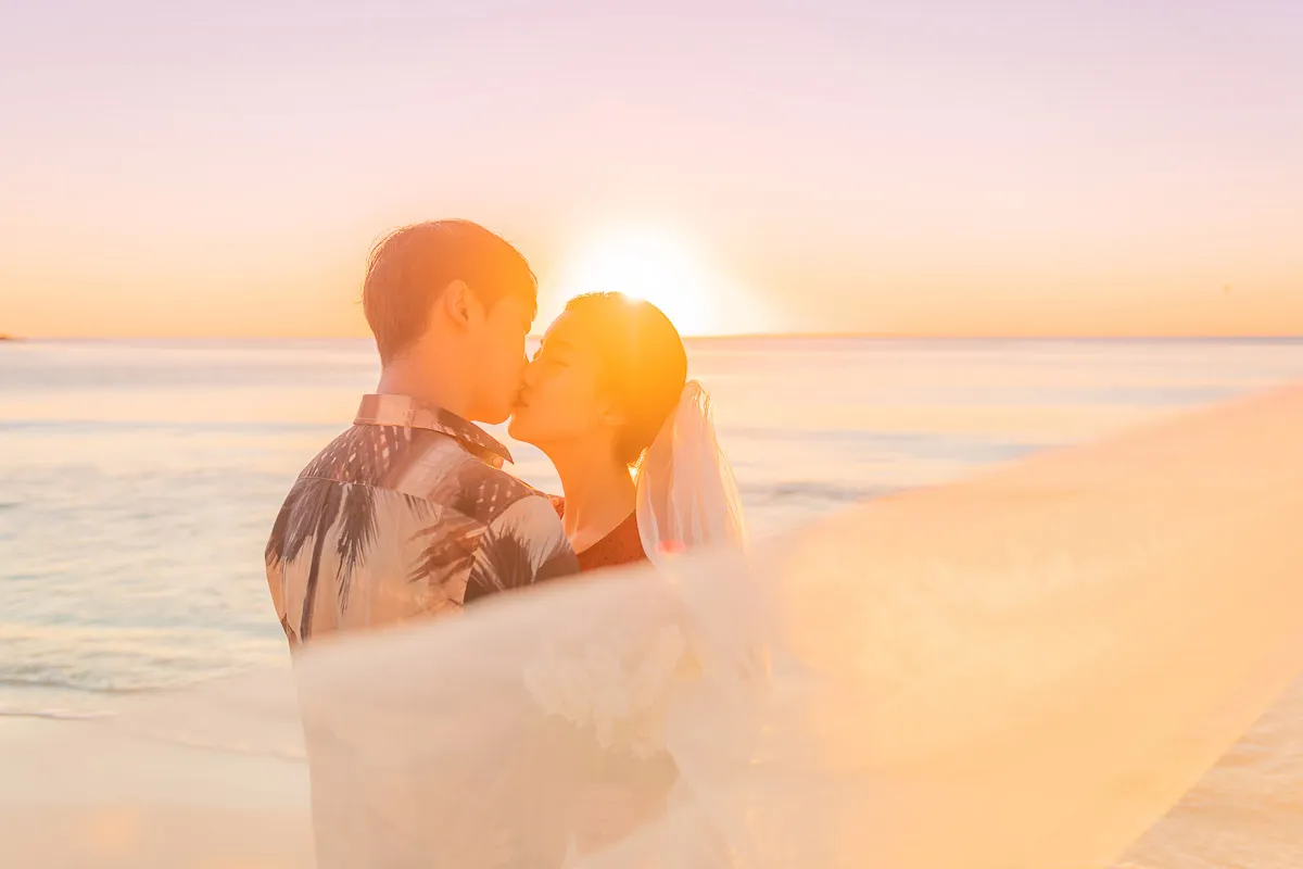 Newlyweds kissing under a veil in golden light