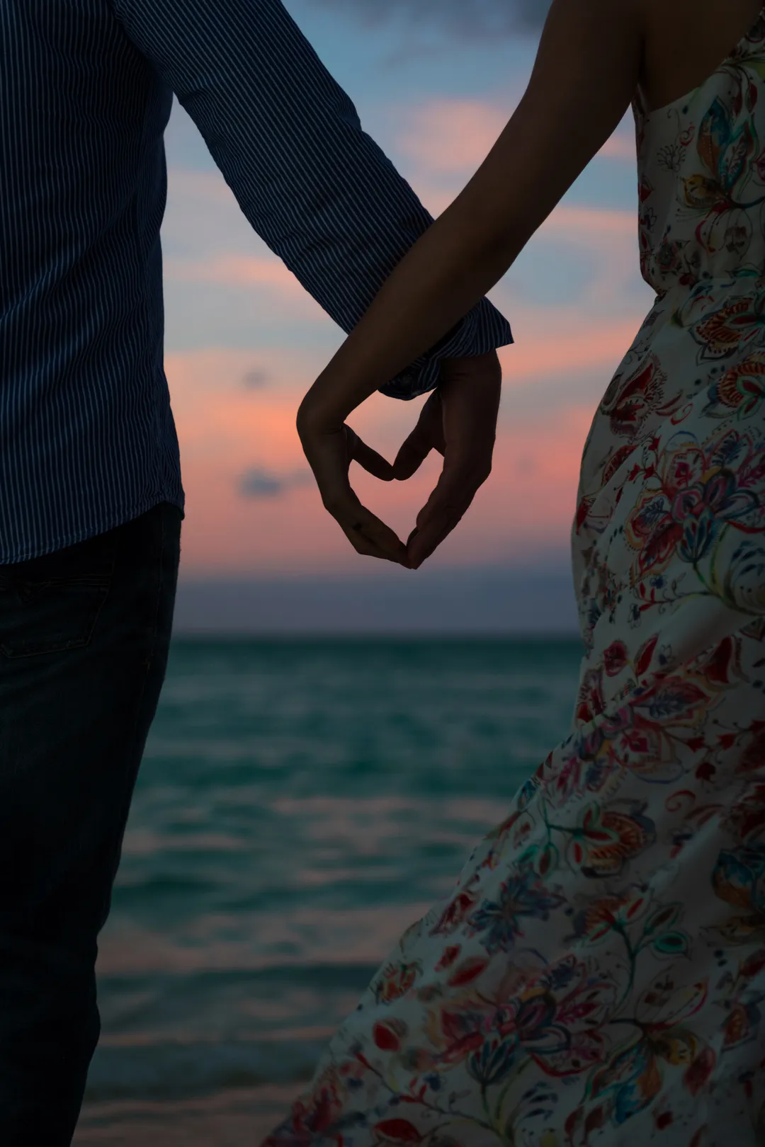 Couple making a heart with their hands against the sunset sea